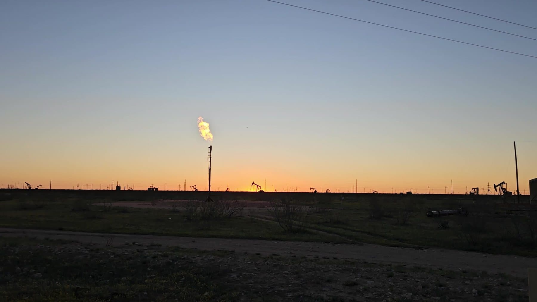 Smokeless flare running at dusk on a Permian Basin pad with pumpjacks on the horizon